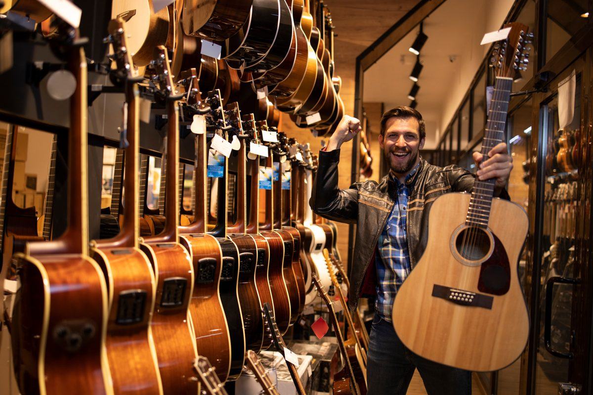 Músico sorridente segurando um violão recém-comprado em uma loja de instrumentos